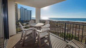 A balcony with a table and chairs, overlooking a beach and a building. - 4th Floor Phoenix VII + 1 Bedroom (Orange Beach)