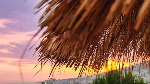 A coastal terrace with a thatched roof, seating area, and a view of the sea at sunset. - Hotel Havana (Sarandë)