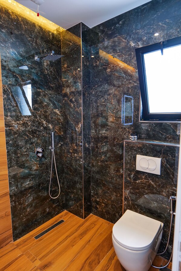 A modern bathroom with a marble wall, a shower, a toilet, and a mirror. - Hotel Havana (Sarandë)