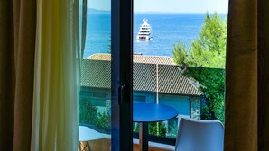 A room with a large sliding glass door leading to a balcony with a view of the sea and a yacht. - Hotel Havana (Sarandë)