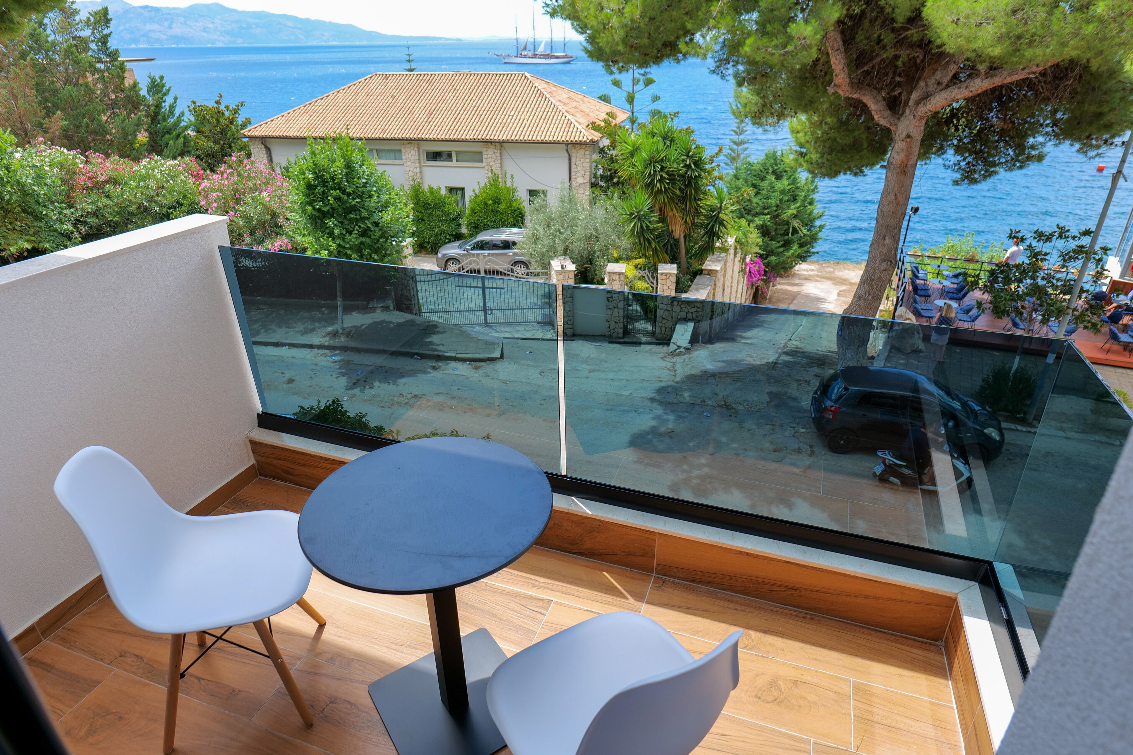 A balcony with a glass railing, two white chairs, and a small round table.