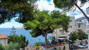 A coastal hotel with outdoor seating overlooking the sea, a paved street, and parked cars. - Hotel Havana (Sarandë)