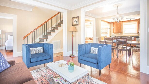 A spacious living room with a staircase, a dining area, and a kitchen. - Downtown Historic District Gem w/ Courtyard + 3 King Beds by Lucky Savannah (Savannah)