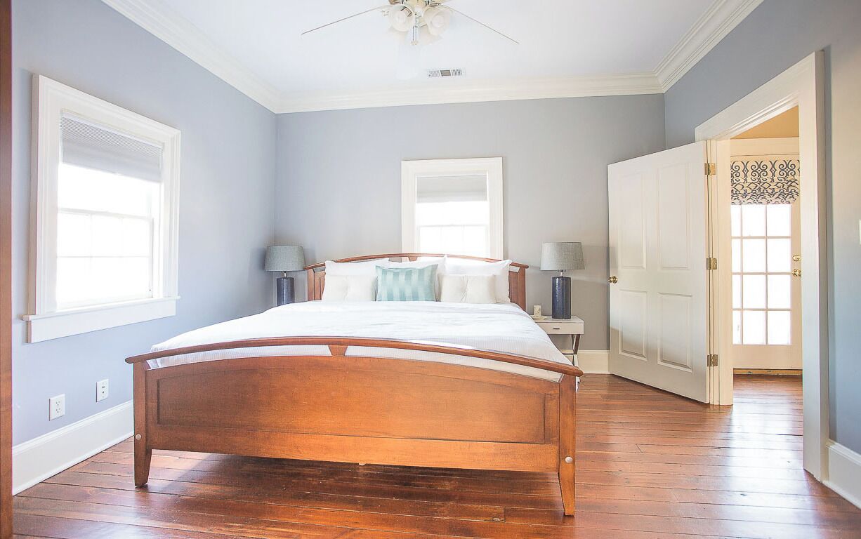 Een slaapkamer met een houten bed, twee nachtkastjes, een plafondventilator en een groot raam.