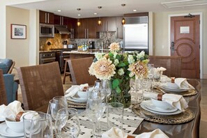 Un coin repas avec une table dressée pour six personnes, un vase de fleurs et une cuisine en arrière-plan.