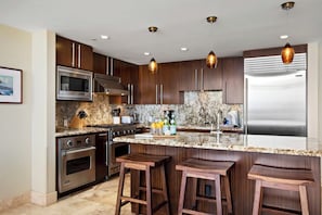 A modern kitchen with stainless steel appliances, wooden cabinets, granite countertops, and pendant lighting. - KBM Resorts | FREE CAR | Honua Kai Hokulani | Ocean view | 3-Bedroom Condo with Ocean Views, Resort Amenities, and Spacious Lanai! HKH-925 (Lahaina)