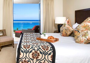 Une chambre d’hôtel avec un lit, une table de chevet, une lampe, un plateau avec des articles pour le petit-déjeuner, une chaise et une vue sur l’océan.