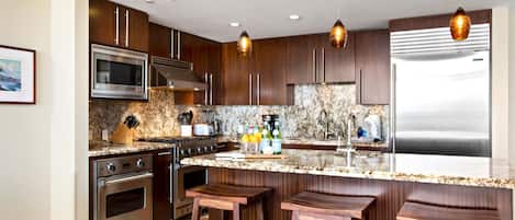 Une cuisine moderne avec des meubles en bois foncé, des appareils en acier inoxydable, un plan de travail en granit et des luminaires suspendus.