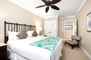 Une chambre à coucher comprenant un lit, une table de chevet, une chaise, un ventilateur de plafond et une porte.