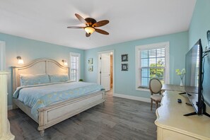 A bedroom with a bed, a ceiling fan, a desk, and a chair.