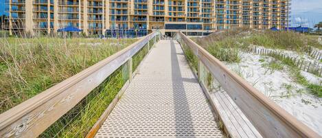 A long, narrow wooden boardwalk leading to a large, multi-story hotel with balconies.