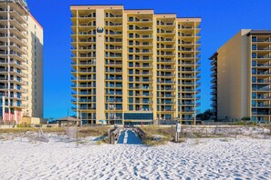 Un hotel a più piani con balconi, vista sulla spiaggia e una spiaggia sabbiosa in primo piano.