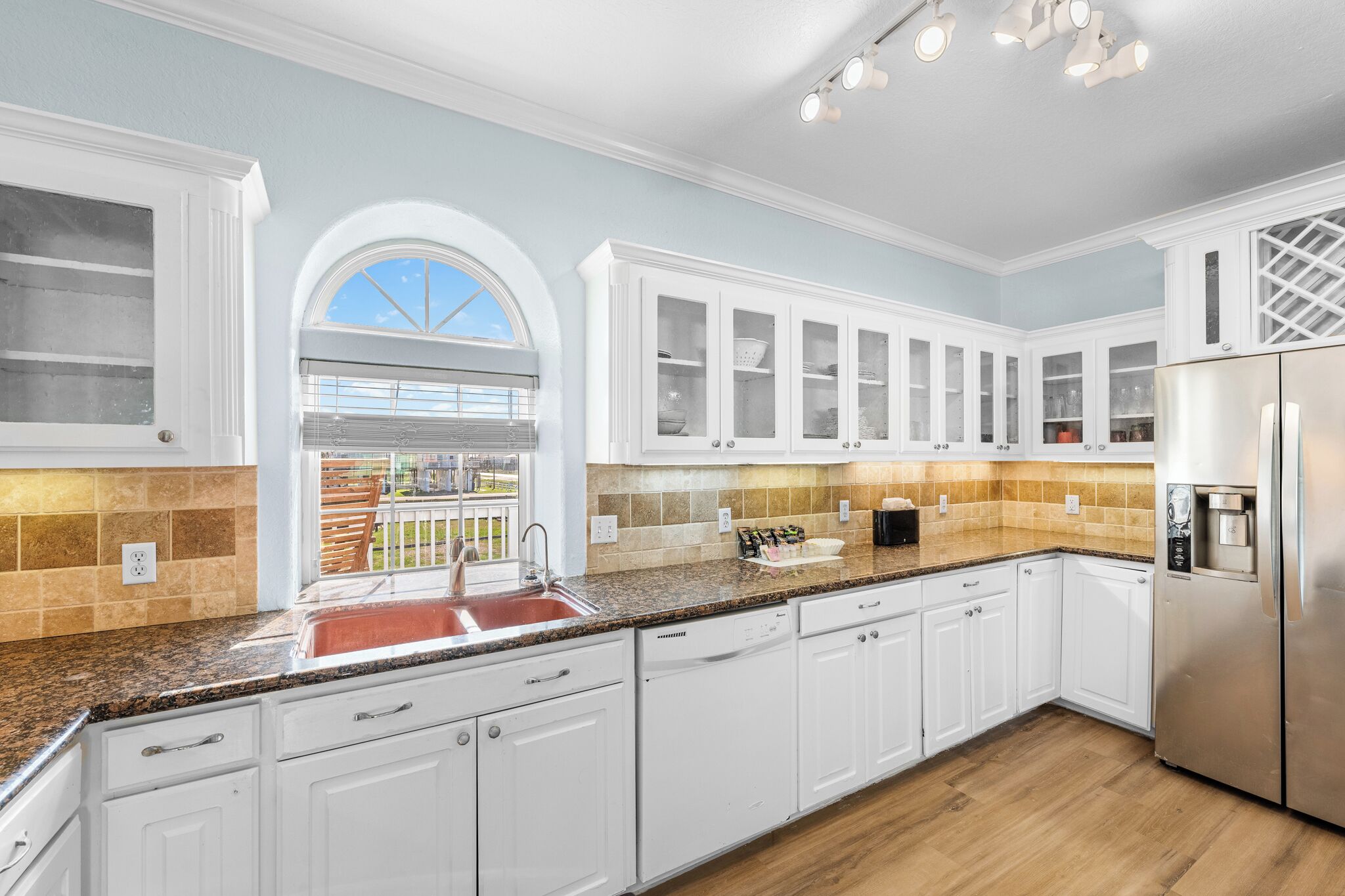 A modern kitchen with white cabinetry, a granite countertop, a stainless steel refrigerator, and a window with a view.