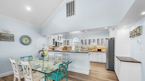 A modern kitchen with white cabinets, a glass dining table, and teal chairs. - Heavenly Sunset...A House With Amazing Views And Just Steps From The Beach (Surfside Beach)