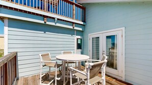 A deck with a round table and four chairs, a wooden railing, and a sliding glass door. - LP11 Ocean View from Deck, Boardwalk, Golf Cart Access (Port Aransas)
