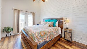 A bedroom with a wooden bed, a ceiling fan, a nightstand with a lamp, and a potted plant. - LP11 Ocean View from Deck, Boardwalk, Golf Cart Access (Port Aransas)