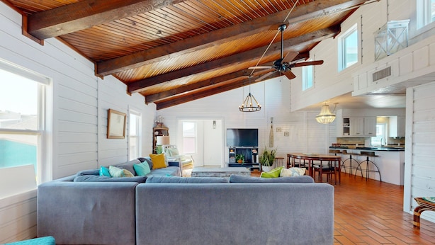 A spacious living area with a large gray sectional sofa, wooden beams on the ceiling, and a kitchen in the background. - LP11 Ocean View from Deck, Boardwalk, Golf Cart Access (Port Aransas)