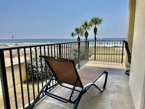 A balcony with a view of the beach, a chair, and a railing.