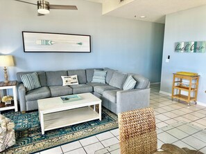 A living room with a grey sectional sofa, a white coffee table, a woven chair, and a small wooden side table.