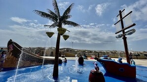 Zona de jocs aquàtics amb una palmera i una estructura amb forma de vaixell pirata.