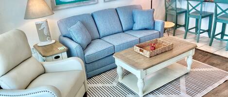 A living room with a light blue sofa, a white armchair, a wooden coffee table, and a patterned rug.
