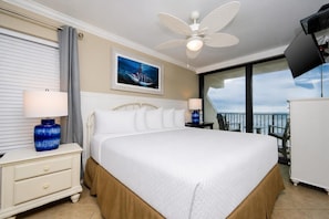 Quarto de hotel com cama grande, ventoinha no teto, pintura de baleia, televisão e varanda com vista para o oceano.
