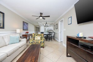 A living room with a sofa, a coffee table, a patterned armchair, a TV stand, and a ceiling fan. - **WEEKLY SPECIALS!** Island Winds West - Beach Front 1BR (Gulf Shores)