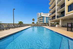 Una piscina con sillas de descanso y un edificio de varios pisos al fondo.