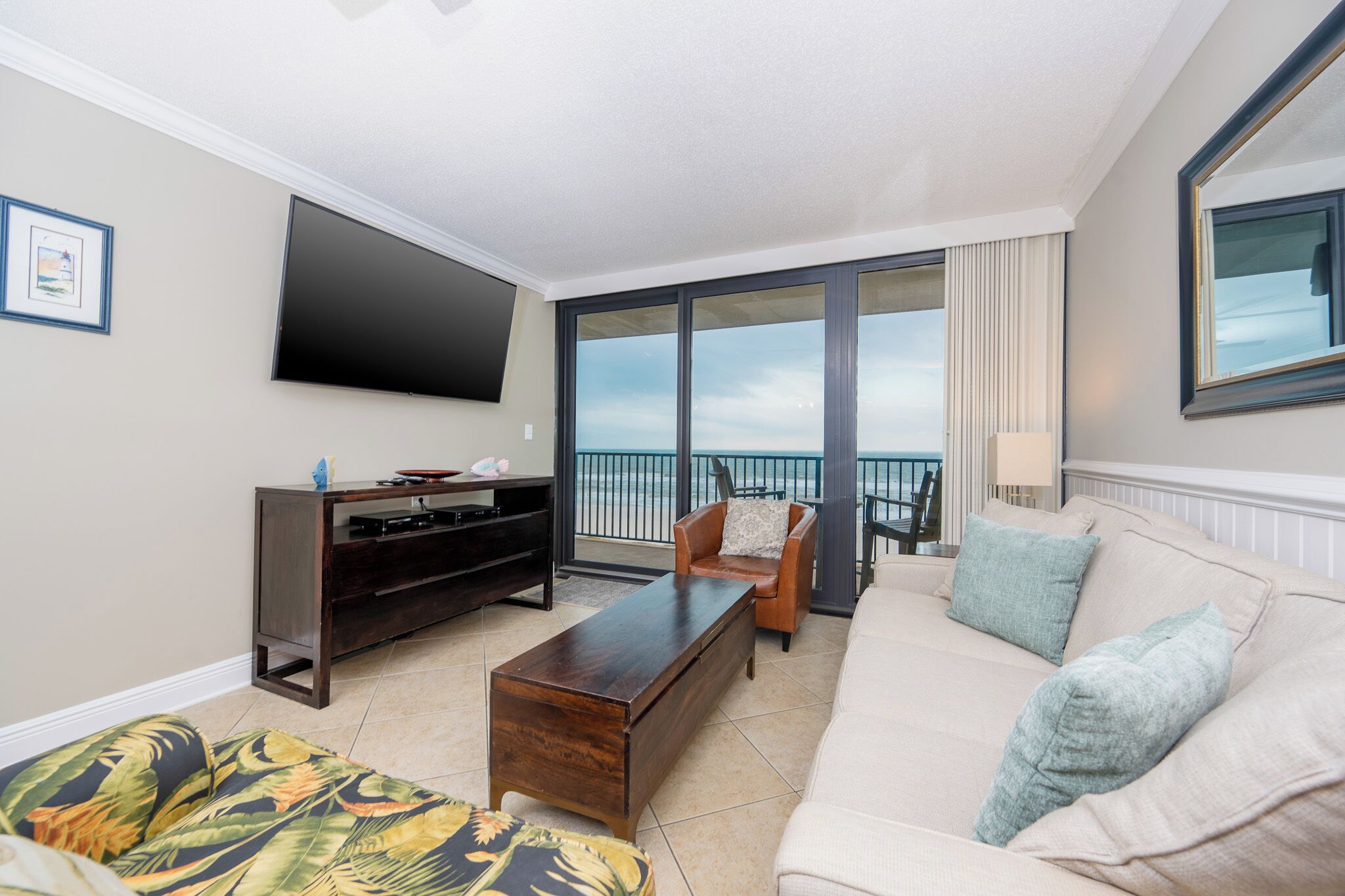 A modern living room with a flat-screen TV, a sofa, a coffee table, and a balcony with a view.