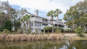 A large, two-story house with a covered porch and a pond in front. - Palmetto Perch - Fully Stocked Wild Dunes Condo with Pool, Close to Beach (Isle of Palms)