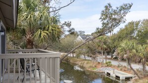 A wooden deck with outdoor furniture, a small pond, and surrounding vegetation. - Palmetto Perch - Fully Stocked Wild Dunes Condo with Pool, Close to Beach (Isle of Palms)