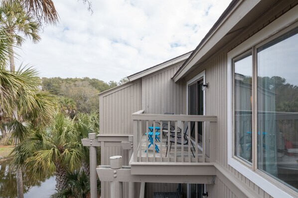 A house with a balcony overlooking a body of water, surrounded by palm trees.