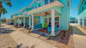Une rangée de maisons turquoise, chacune dotée d’un porche abrité, de petites plantes et d’un tapis rouge.