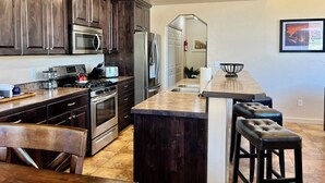Uma cozinha moderna com armários de madeira escura, eletrodomésticos de aço inoxidável, bancada de granito e uma ilha central com banquetas.
