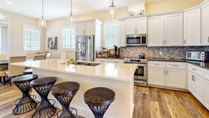 A modern kitchen with white cabinets, a large island with stools, stainless steel appliances, and pendant lighting. - Luxe Palmilla Beach Resort house with pool, dining & private golf cart (Port Aransas)