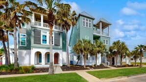 A two-story house with a balcony and a covered porch, surrounded by palm trees and a well-maintained lawn. - Luxe Palmilla Beach Resort house with pool, dining & private golf cart (Port Aransas)