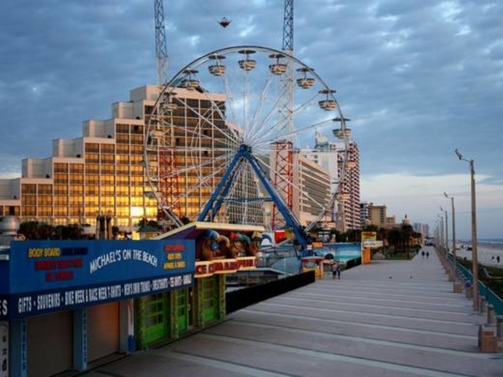 Une promenade en bord de mer avec une grande roue et un immeuble à plusieurs étages doté de balcons.
