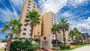 A hotel with a sign reading "Sanibel," surrounded by palm trees and a clear sky. - Direct Oceanfront - Heated Pool & Hot Tub (Daytona Beach Shores)