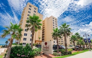 A hotel with a sign reading "Sanibel," surrounded by palm trees and a clear sky.