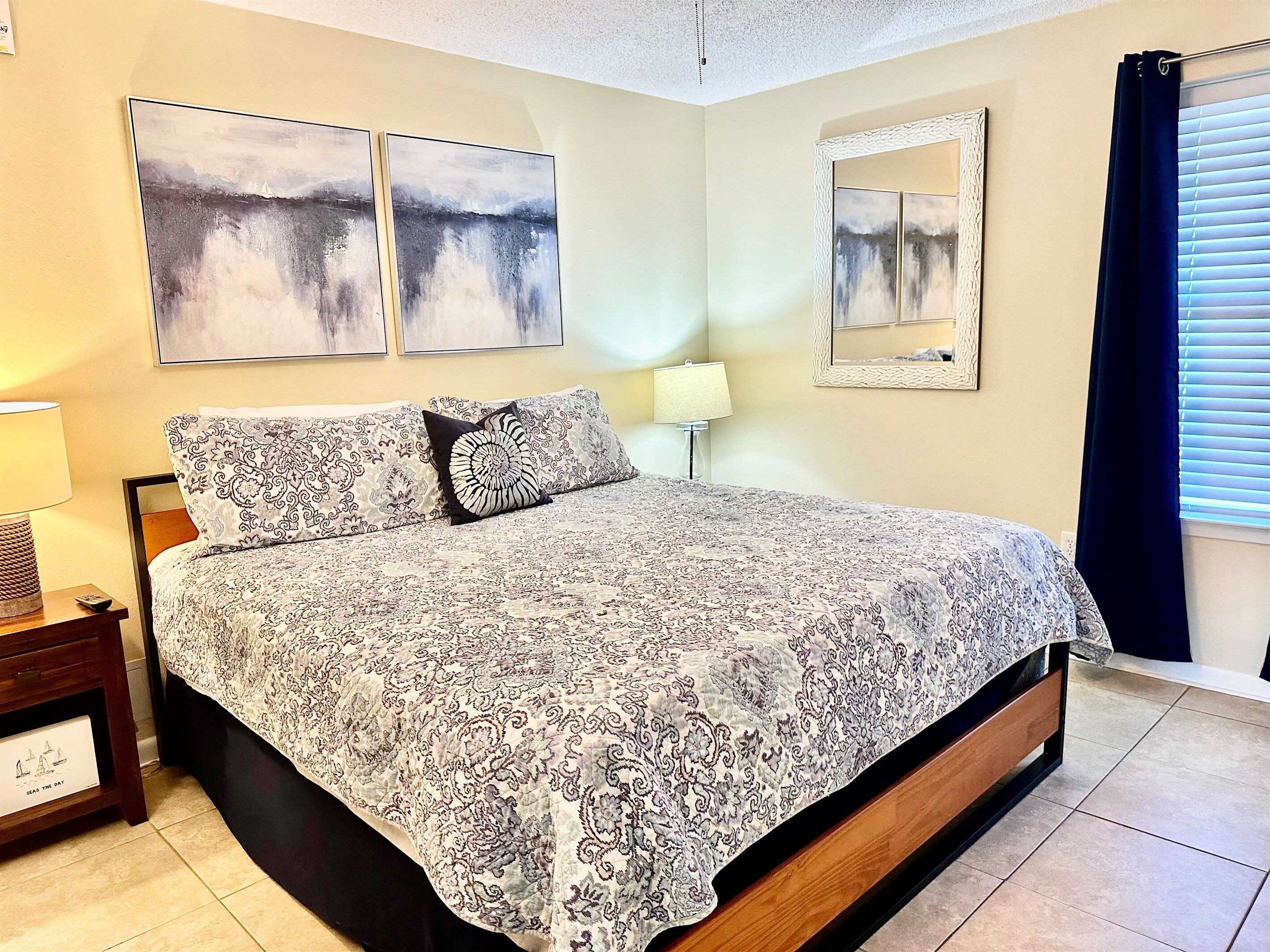A bedroom with a bed, a nightstand, a lamp, and two wall-mounted paintings.