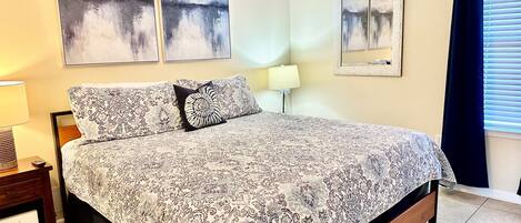 A bedroom with a bed, a nightstand, a lamp, and two wall-mounted paintings.