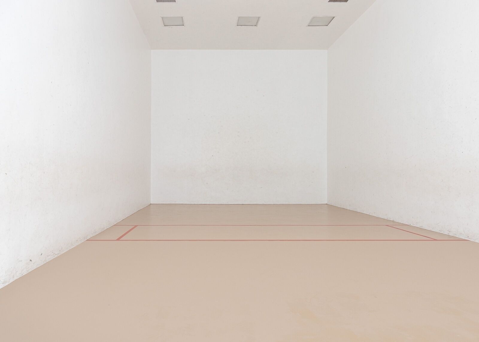 A clean, empty room with white walls and a light-colored floor, featuring a visible red line marking the playing area.