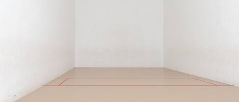 A clean, empty room with white walls and a light-colored floor, featuring a visible red line marking the playing area.