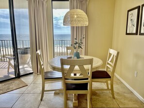 Enjoy the ocean view from this room's large window, featuring a round table with two chairs and a vase with a plant.
