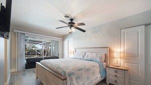A bedroom with a bed, a nightstand, a ceiling fan, and a sliding glass door leading to a balcony. - Canal Escape, Boat Rental, Hot Tub, Fishing (Cape Coral)