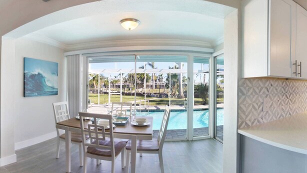 A modern kitchen with a view of a swimming pool and a dining area with a table and chairs. - Canal Escape, Boat Rental, Hot Tub, Fishing (Cape Coral)