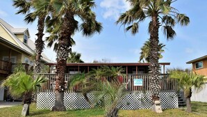 A building with a fenced front yard, palm trees, and a sign indicating a rental property.