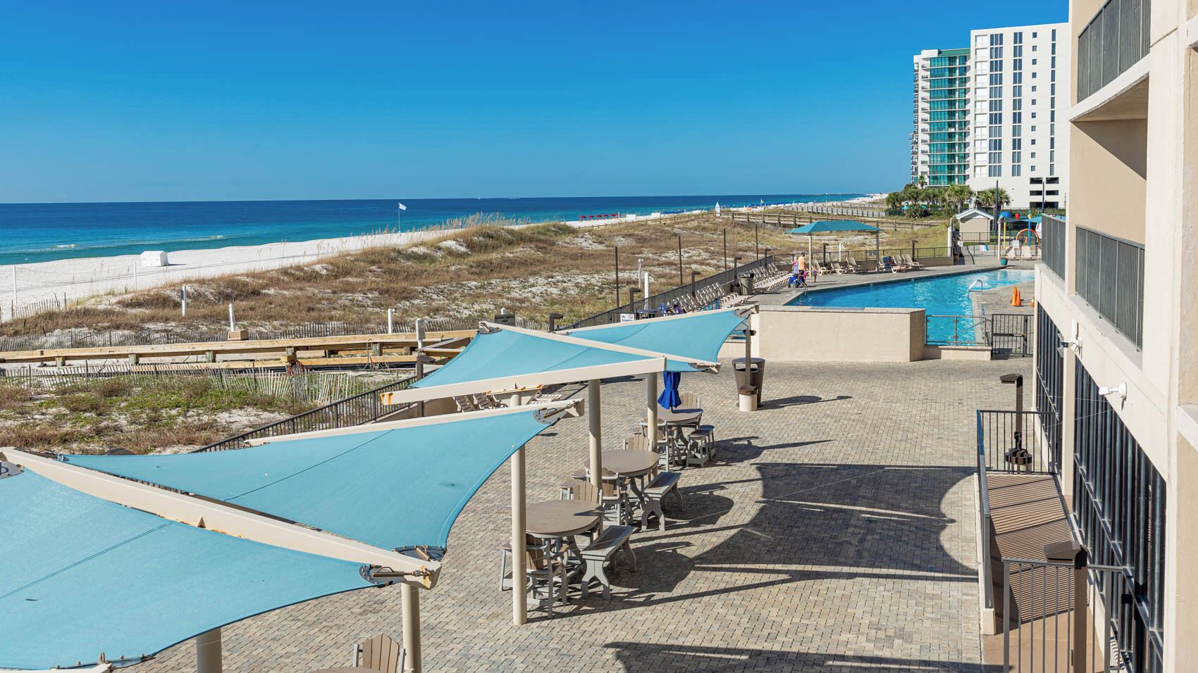 A rooftop pool area with umbrellas, lounge chairs, and a view of the beach and ocean.