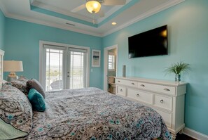 Une chambre à coucher avec un lit, une commode, un téléviseur et un ventilateur de plafond.
