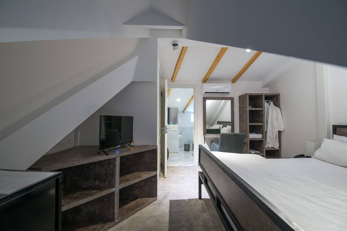 A bedroom with a bed, a TV, a wardrobe, and a bathroom visible through an open door.